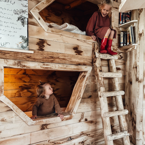 Deux enfants jouent dans une chambre en bois avec lits superposés, Hobbit House de Cosy Cabins, forêt de Limbourg, Belgique.