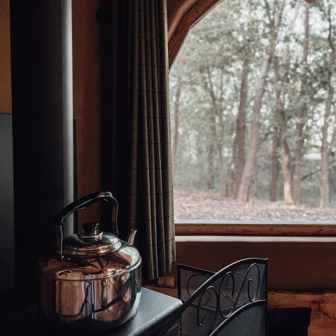 Im Inneren des Hobbit House in Cosy Cabins Limburg, Belgien, steht ein Teekessel vor einem Wald-Fenster.