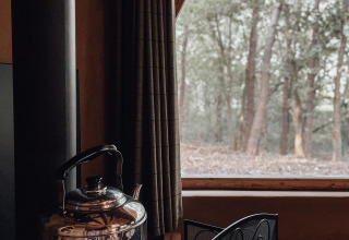 Dentro de Hobbit House en Cosy Cabins, Limburg, Bélgica, una tetera está junto a la ventana con bosque.