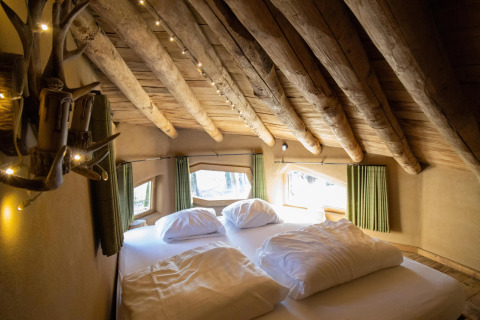 Dormitorio en Hobbit House de Cosy Cabins, con vigas de madera y ventanas al bosque en Limburg, Bélgica.