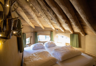 Soveværelse i Hobbit House-lodgen ved Cosy Cabins, med træloft og vinduer i skoven i Limburg, Belgien.