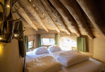 Slaapkamer in Hobbit House bij Cosy Cabins, met houten balken en ramen in het Limburgse bos, België.