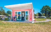 Tres personas sentadas fuera de una tiny house Valley Chalet rosa en Holiday Park Ackersate, Países Bajos.