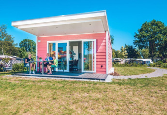 Drie personen zitten voor een roze Valley Chalet tiny house op Vakantiepark Ackersate in Nederland.