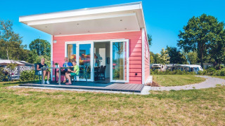 Drie personen zitten voor een roze Valley Chalet tiny house op Vakantiepark Ackersate in Nederland.