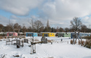 Bunte Tiny Houses im Schnee bei Valley Chalet, Holiday park Ackersate, Niederlande, mit Spielplatz vorne.