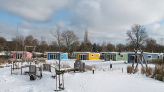 Kleurige tiny houses in sneeuw bij Valley Chalet, Holiday park Ackersate, Nederland, speeltuin op de voorgrond.