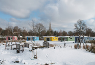 Colorful tiny houses in snow at Valley Chalet, Holiday park Ackersate, Netherlands, playground in front.