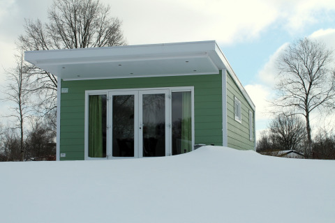 Una tiny house verde en Valley Chalet, cubierta de nieve, en Holiday park Ackersate, Países Bajos, en invierno.