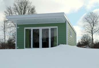 A green tiny house at Valley Chalet, covered in snow, located at Holiday park Ackersate in the Netherlands.
