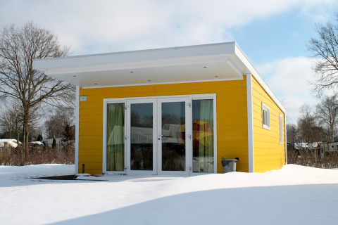 Tiny house Valley Chalet gialla nella neve al Holiday park Ackersate, Paesi Bassi, dal design moderno.