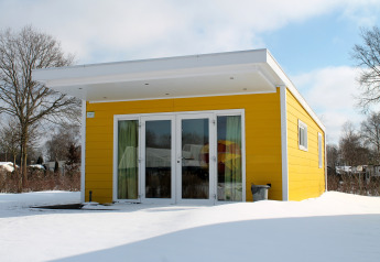 Gele Valley Chalet tiny house in de sneeuw op Vakantiepark Ackersate in Nederland, met modern ontwerp.