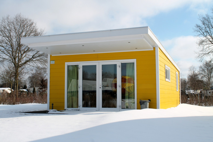 Gele Valley Chalet tiny house in de sneeuw op Vakantiepark Ackersate in Nederland, met modern ontwerp.
