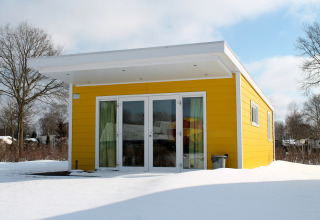 Gele Valley Chalet tiny house in de sneeuw op vakantiepark Ackersate in Nederland met strakke lijnen.