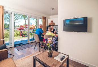 Gezin aan tafel in Valley Chalet op Vakantiepark Ackersate, met buiten zicht op waterglijbanen.
