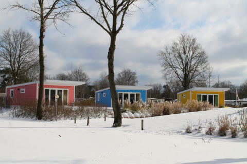 Pequeñas casas coloridas en Valley Chalet con nieve en Holiday park Ackersate, Países Bajos, en invierno.