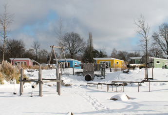 Casas diminutas coloridas y parque infantil nevado en Valley Chalet, Holiday park Ackersate, Países Bajos.