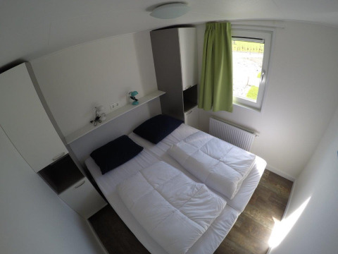 Slaapkamer in Valley Chalet bij vakantiepark Ackersate, Nederland, met twee bedden en groene gordijn bij raam.