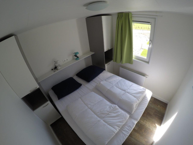 Slaapkamer in Valley Chalet bij vakantiepark Ackersate, Nederland, met twee bedden en groene gordijn bij raam.