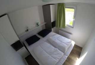 Slaapkamer in Valley Chalet bij vakantiepark Ackersate, Nederland, met twee bedden en groene gordijn bij raam.