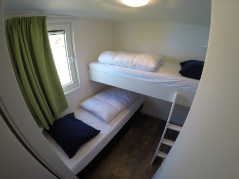 Habitación pequeña con literas, cortinas verdes y suelo de madera en Valley Chalet, Holiday park Ackersate, Países Bajos.