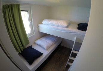 Habitación pequeña con literas, cortinas verdes y suelo de madera en Valley Chalet, Holiday park Ackersate, Países Bajos.