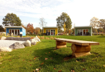 Kleurige Valley Chalet tiny houses in Holiday park Ackersate, Nederland, met gras, stenen en houten bank.