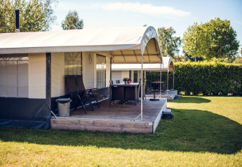 Safari-telt ved Holiday park Ackersate i Holland med træterrasse, stole og grøn have om sommeren.