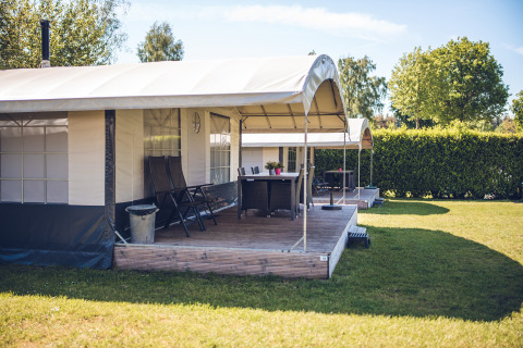 Safari-telt ved Holiday park Ackersate i Holland med træterrasse, stole og grøn have om sommeren.