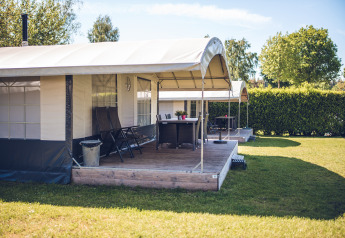 Safari-Zeltvilla im Ferienpark Ackersate in den Niederlanden mit Veranda und Garten im Sonnenschein.
