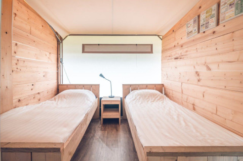 Interieur van een Tentvilla safaritent in vakantiepark Ackersate met twee eenpersoonsbedden en houten muren.