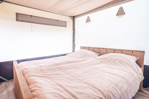 Chambre lumineuse d'une tente safari au Holiday park Ackersate, Pays-Bas, avec lit double confortable.
