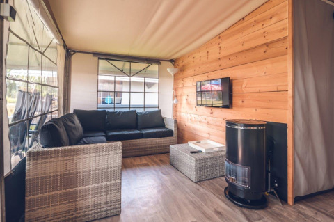 Modern safari tent living room at Holiday park Ackersate, Netherlands, featuring sofa, TV, and wood walls.