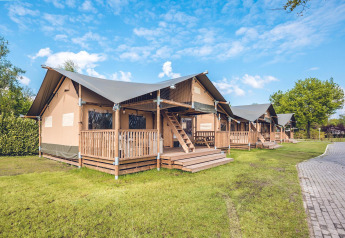 Safaritent 'Red Deer' op Vakantiepark Ackersate in Nederland, houten veranda, grasveld en zonnige lucht.