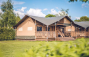 Tenda safari 'Red Deer' all’Holiday park Ackersate nei Paesi Bassi, veranda in legno e prato verde estivo.