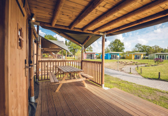 Vista desde el porche de madera de la tienda Safari 'Red Deer' en Holiday park Ackersate, Países Bajos, con cabañas.