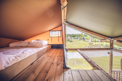 Innenansicht des Safari-Zelts 'Red Deer' im Ferienpark Ackersate in den Niederlanden mit Bett und Netz.