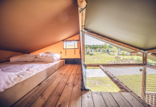 Innenansicht des Safari-Zelts 'Red Deer' im Ferienpark Ackersate in den Niederlanden mit Bett und Netz.