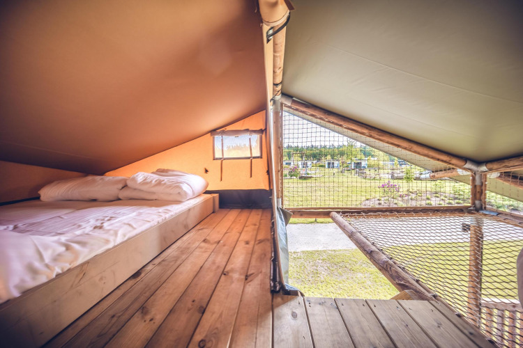 Interieur van safaritent 'Red Deer' op Vakantiepark Ackersate in Nederland, met bed en net zichtbaar.