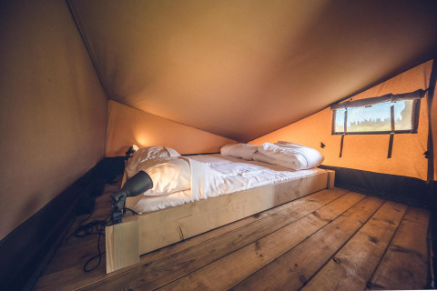 Interiør af Safari tent 'Red Deer' på Holiday park Ackersate i Holland med en hyggelig seng og trægulv.