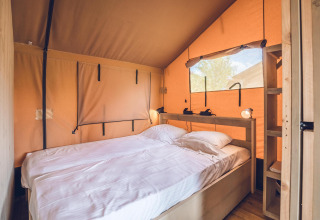 Interior de la tienda safari 'Red Deer' en Holiday park Ackersate, con cama doble y detalles en madera clara.
