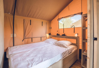 Interior view of Safari tent 'Red Deer' at Holiday park Ackersate, featuring a cozy double bed and wood décor.