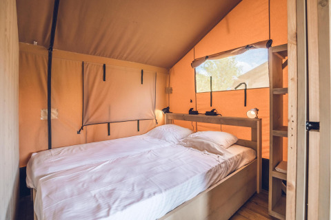 Innenansicht des Safari-Zeltes 'Red Deer' im Ferienpark Ackersate mit gemütlichem Bett und Holzmöbeln.