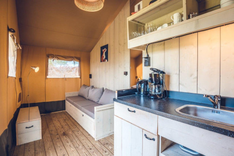 Interieur van safaritent 'Vos' op vakantiepark Ackersate in Nederland met zetel en keukenhoek.