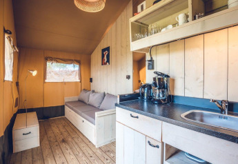 Interieur van safaritent 'Vos' op vakantiepark Ackersate in Nederland met bank en kitchenette.