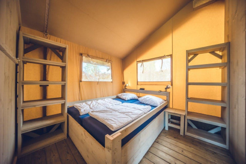 Slaapkamer in safari tent 'Vos' op vakantiepark Ackersate in Nederland, met bed en open kasten.
