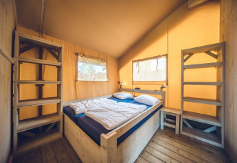 Slaapkamer in safaritent 'Vos' op vakantiepark Ackersate in Nederland, met tweepersoonsbed en planken.