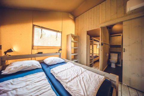 Binnenzicht van safaritent 'Vos' in vakantiepark Ackersate, Nederland, met bedden en een badkamer zichtbaar.