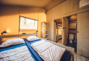 Interieur van safaritent 'Vos' bij vakantiepark Ackersate in Nederland, met bedden en badkamer in beeld.