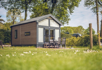 Knus tiny house op Vakantiepark Ackersate in Nederland, omgeven door groen gras en tuinmeubilair buiten.